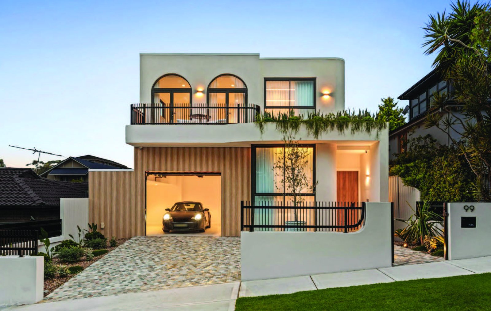 Contemporary rendered home with arched windows and a timber-clad garage at dusk